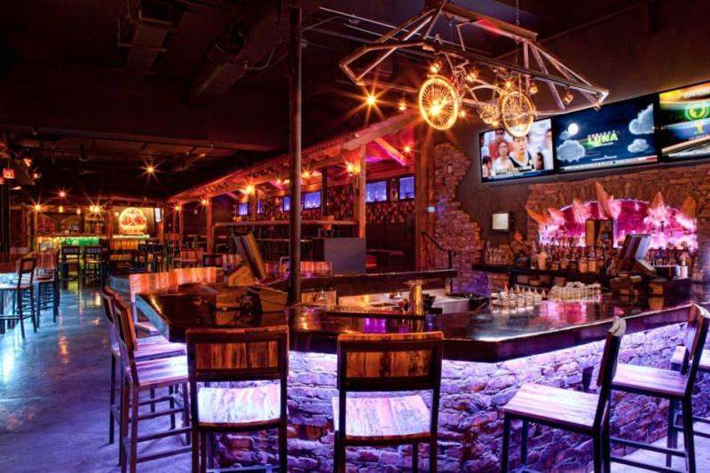 Club interior lit in red and purple with bar seating and mounted screens