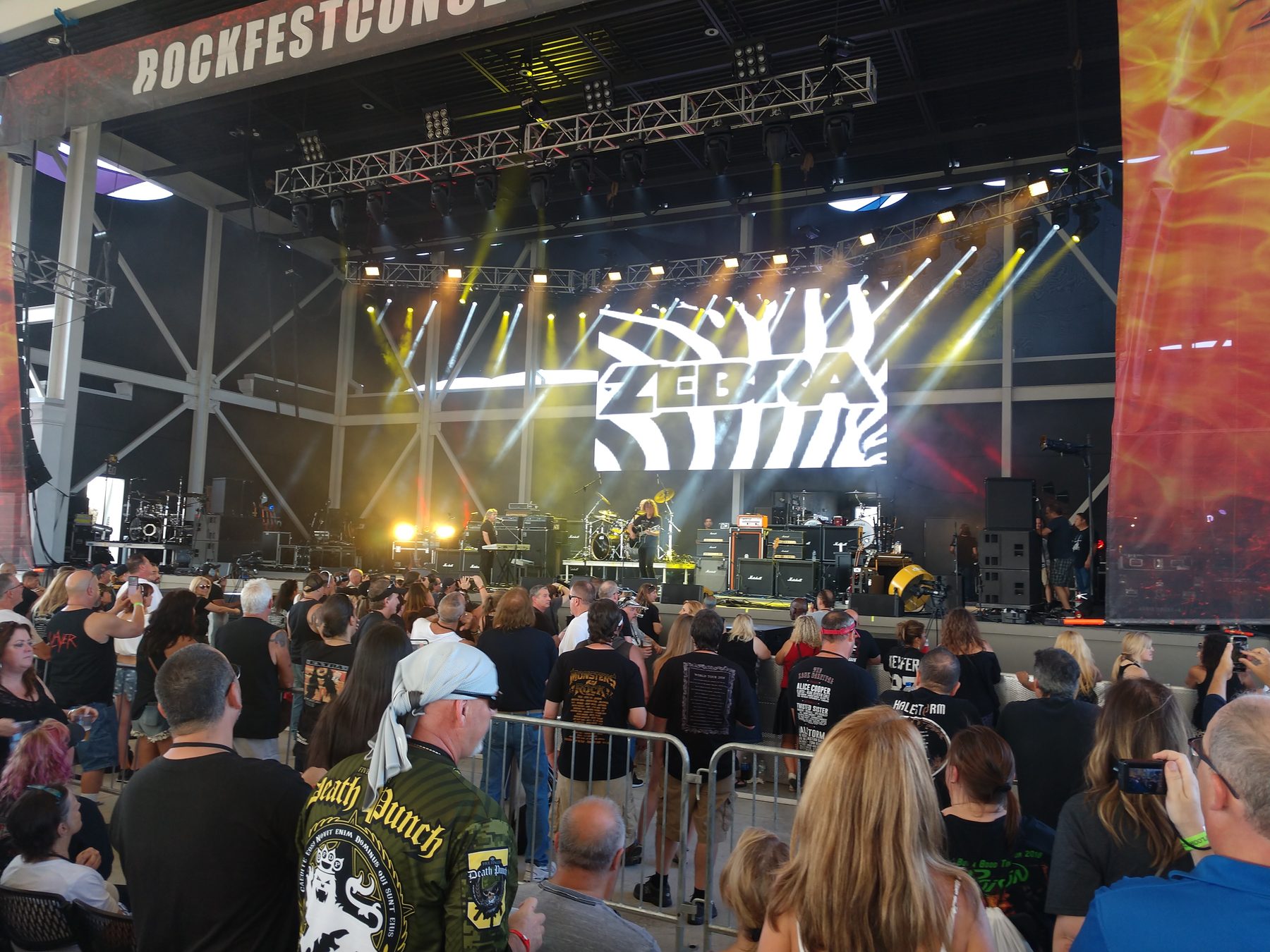 Outdoor festival stage with lighting truss, line arrays and an audience at the barricade