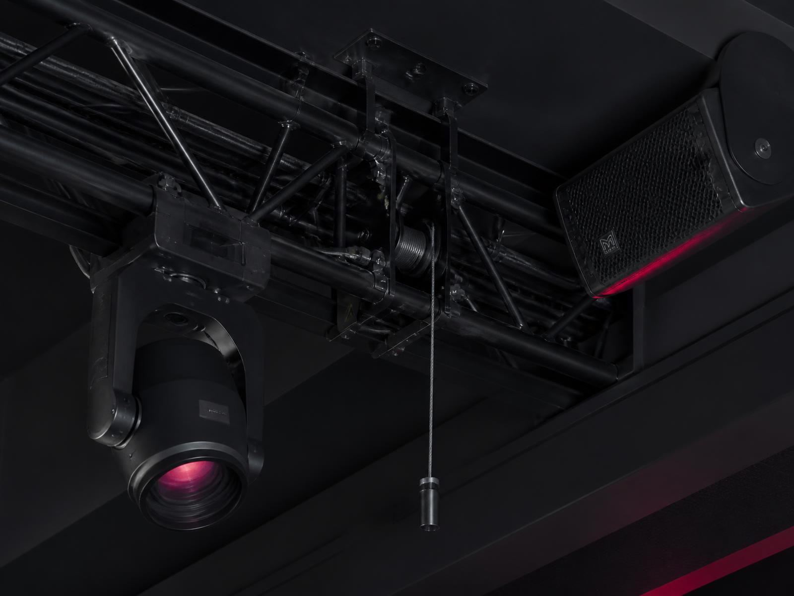 Close detail of an installed moving-head fixture, loudspeaker, rigging motor and dressed cabling in a venue ceiling