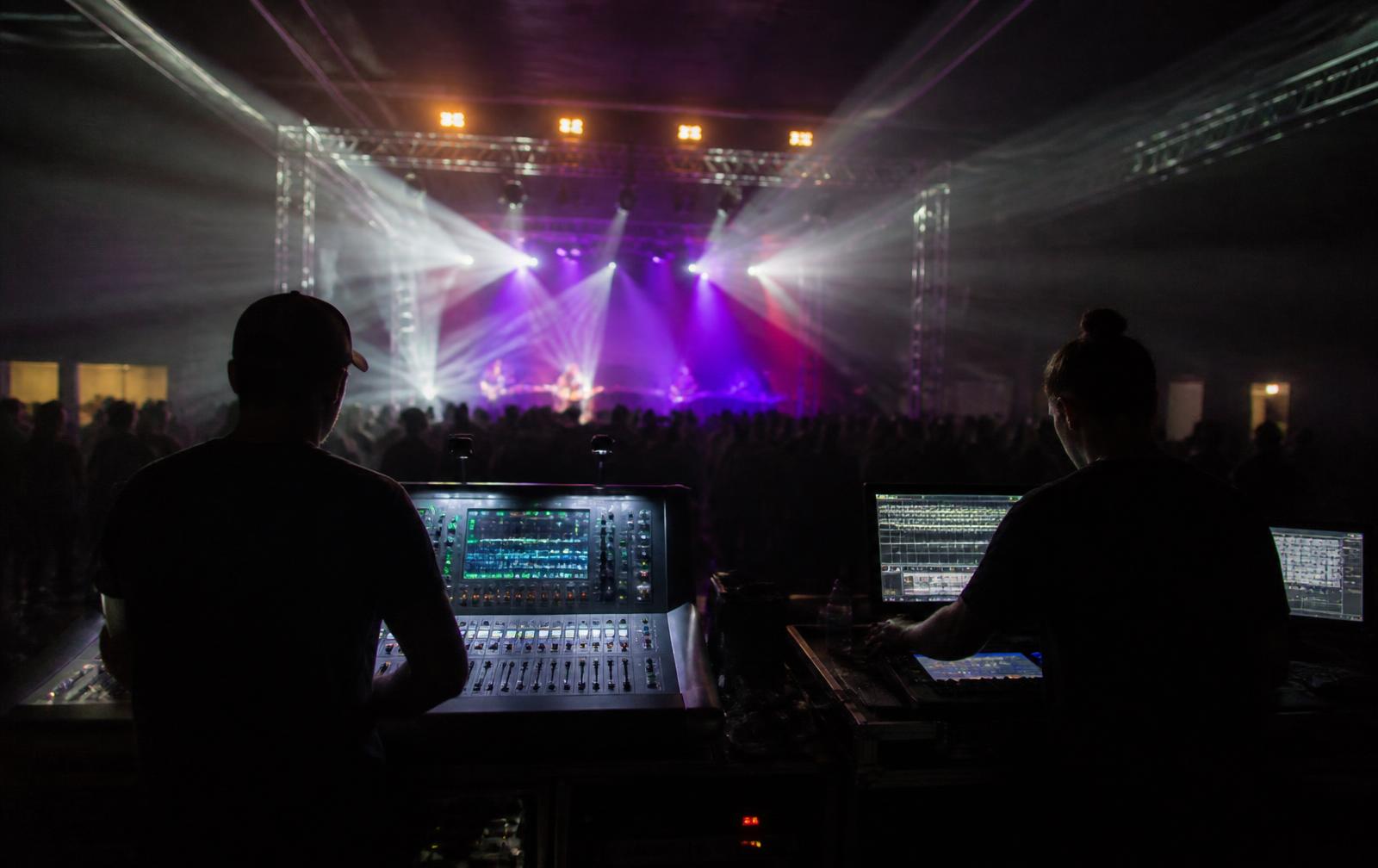 Audio engineer and lighting operator working side by side at front of house during a live show