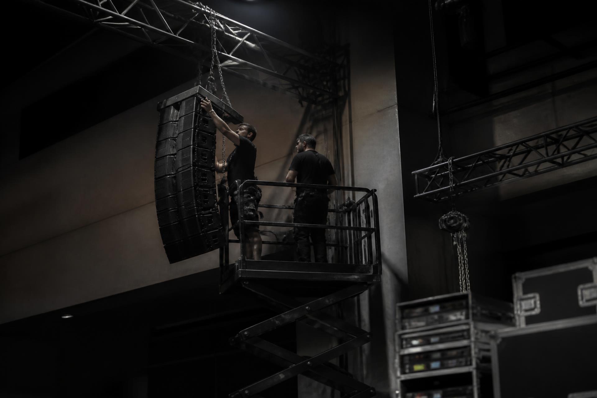 Technicians installing a line array loudspeaker and lighting truss in a venue