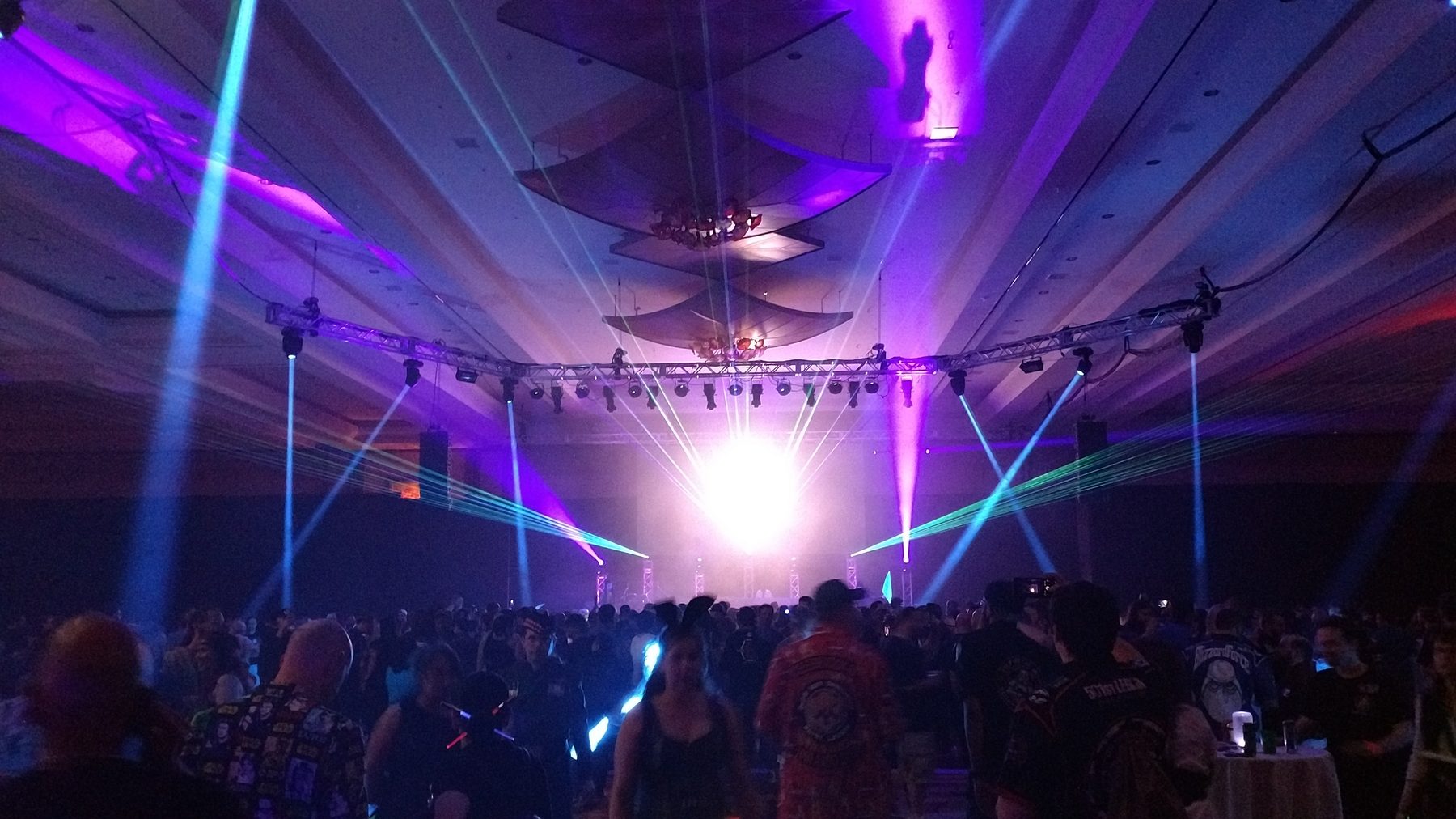 Large event room filled with laser and lighting effects above a crowd